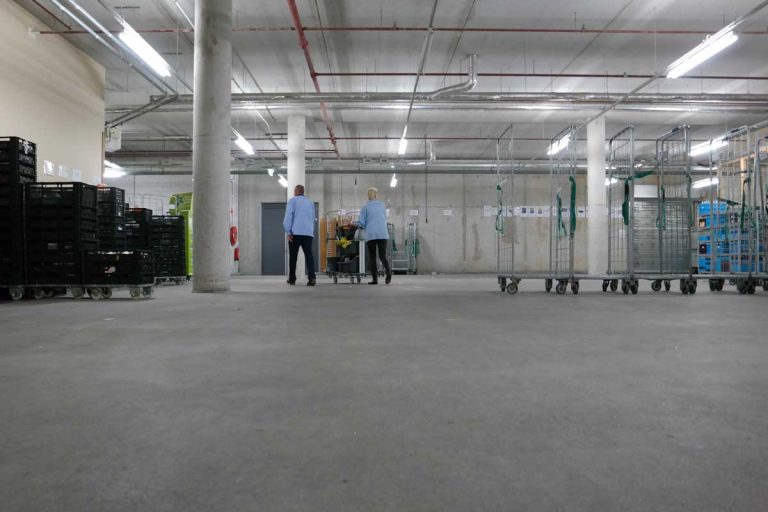 Warehouse workers moving carts in a large storage facility on a concrete floor